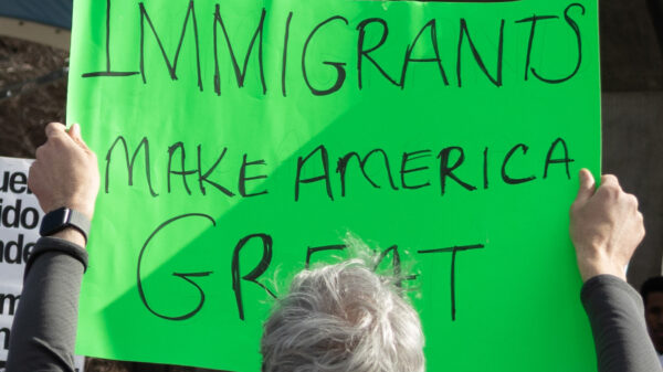Photo of a person at a protest holding up a green sign with the text Immigrants make America great