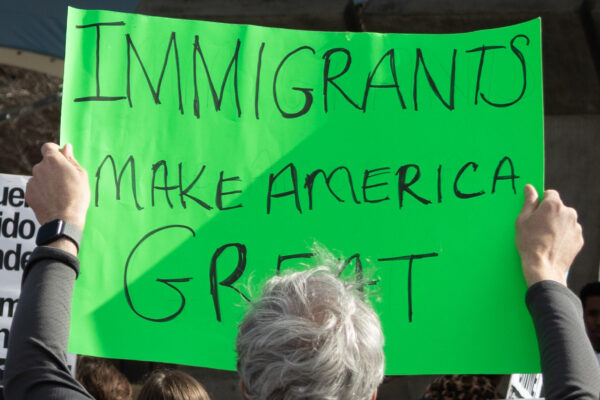 Photo of a person at a protest holding up a green sign with the text Immigrants make America great