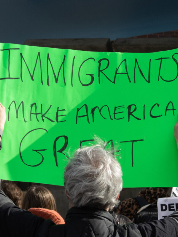 Photo of a person at a protest holding up a green sign with the text Immigrants make America great