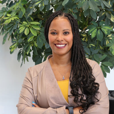 Headshot photo of Erica Tinsley, smiling, in front of a green leafy plant