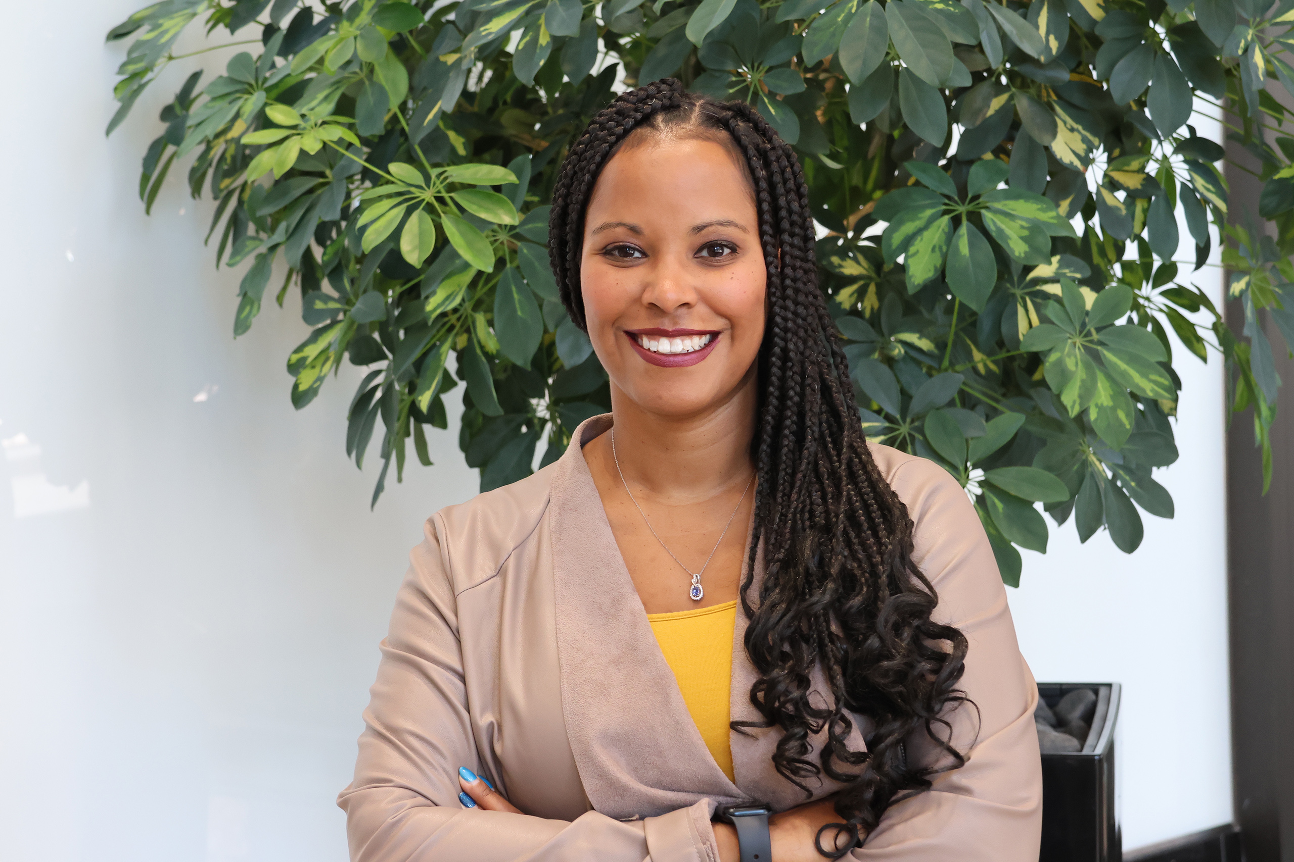 Headshot photo of Erica Tinsley, smiling, in front of a green leafy plant