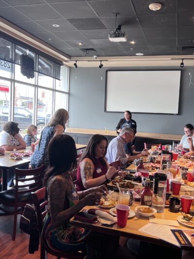 Photo of activists gathered around tables with food watching a presentation