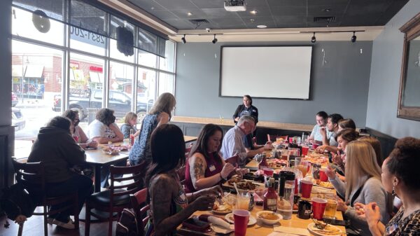 Photo of activists gathered around tables with food watching a presentation