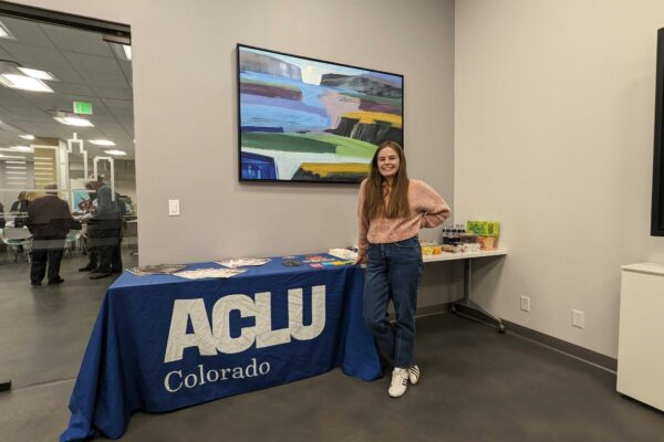 An intern stands in front of a table with a blue ACLU of Colorado tablecloth and an assortment of printed materials