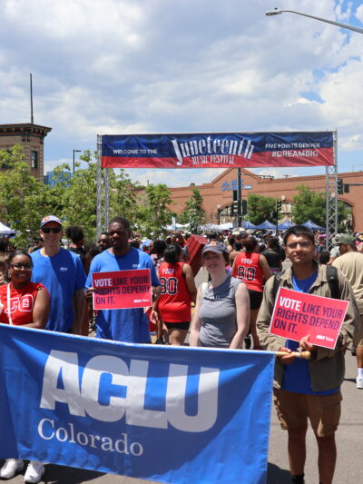 Photo of people in a parade holding a banner that says ACLU Colorado in front of a larger banner that says Juneteenth