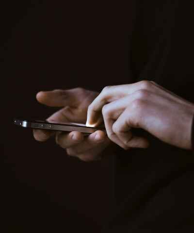 Photo of hands holding a smartphone in a dark room with a dark background