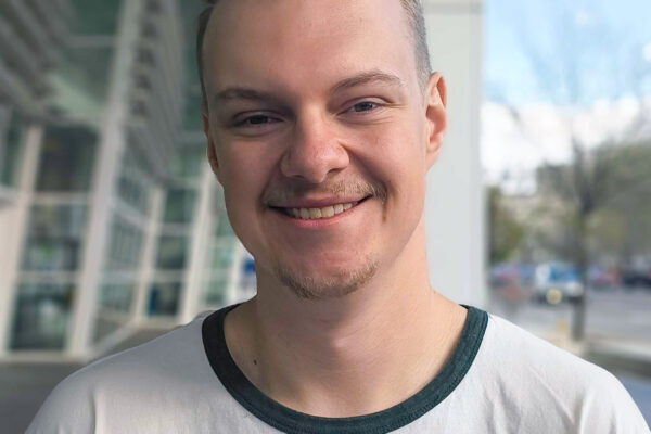 Headshot photo of Ivan, smiling, standing in front of building with large glass windows