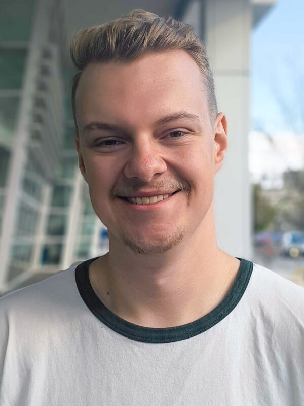Headshot photo of Ivan, smiling, standing in front of building with large glass windows
