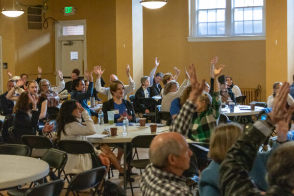Photo of supporters at ACLU of Colorado's lobby day sitting around tables with their hands raised