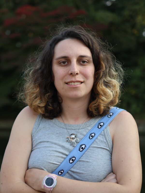 Photo of Aisha Nammari, arms crossed, smiling, in front of plants.