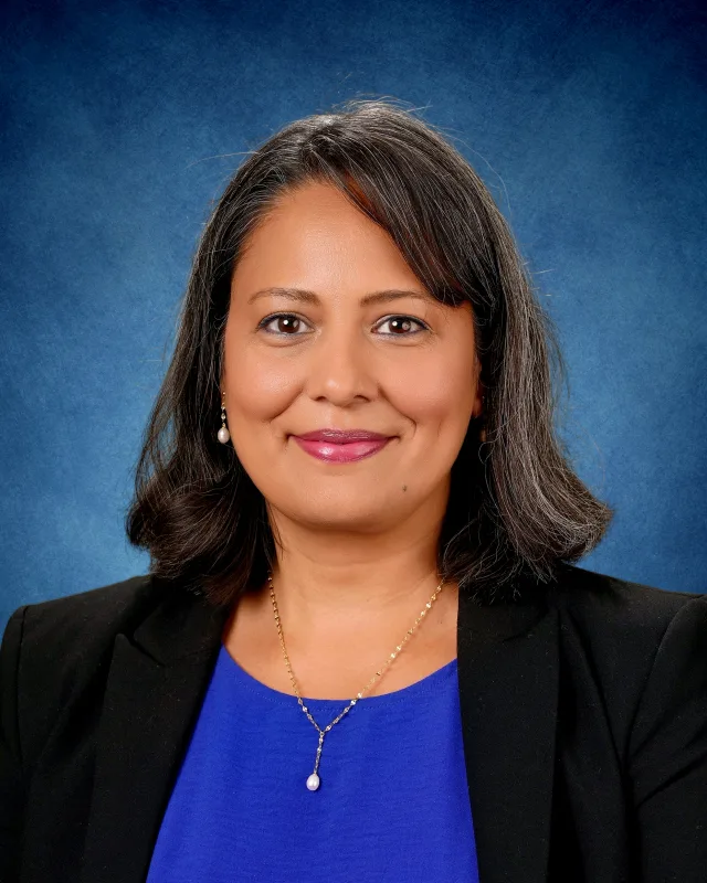 Headshot photo of Ishmeet Kalra smiling with a blue background