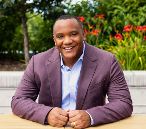 Photo of Michael Smith smiling, with flowers and plants in the background.