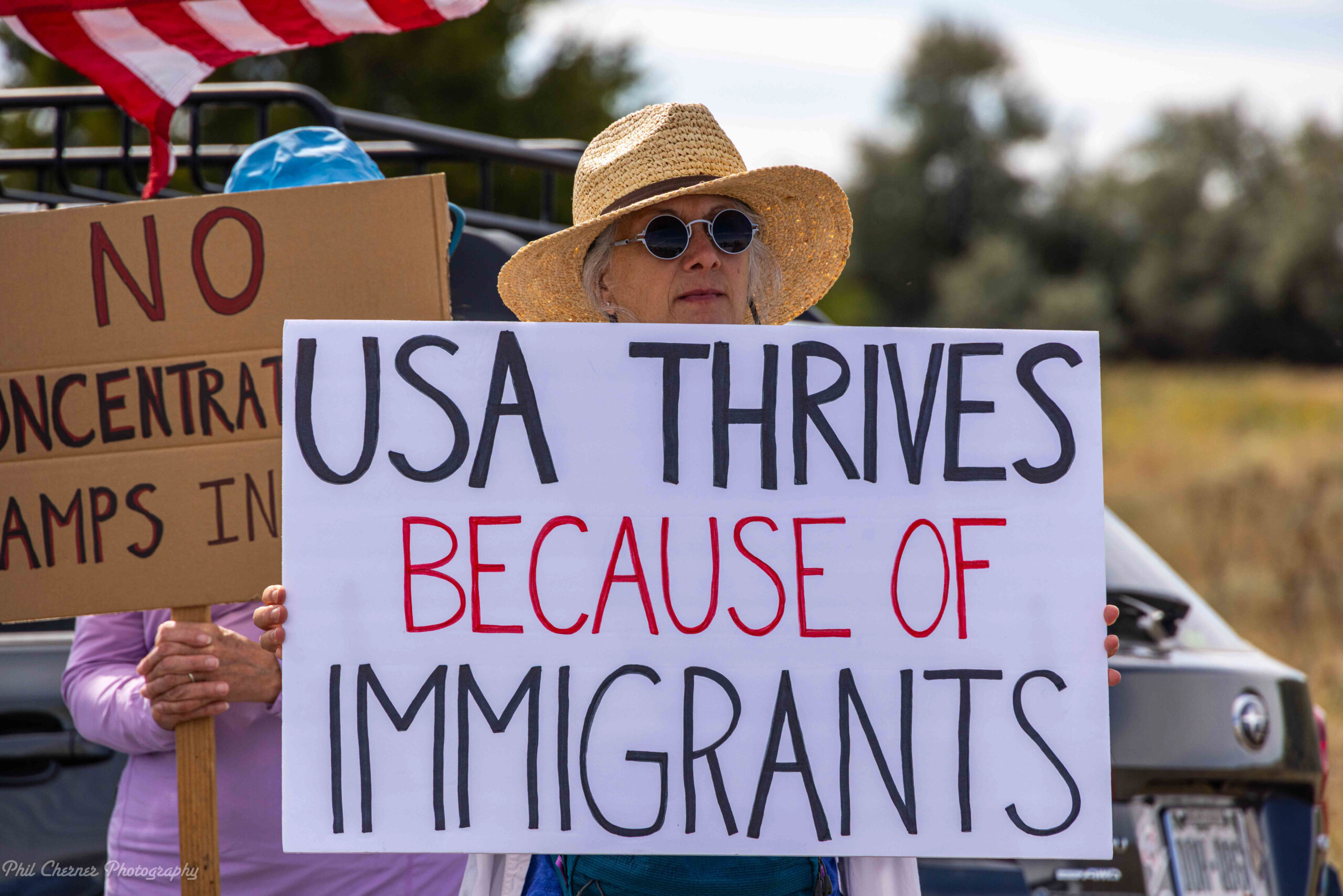 Photo of a protestor holding a sign with the text USA thrives because of immigrants.