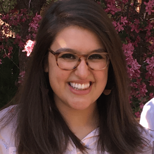 Headshot photo of Ariane Frosh, smiling, with pink flowers in the background