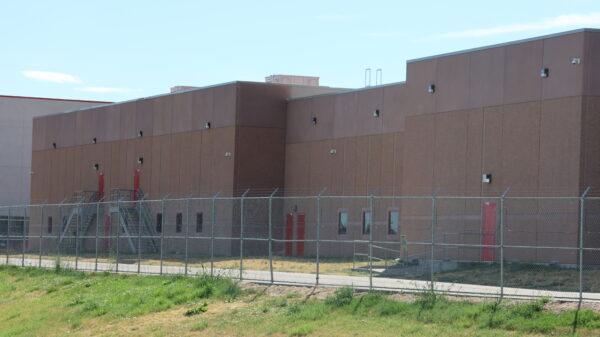 Photo: outside of the ICE facility in Aurora, CO with barbed wire fences and brown concrete walls.