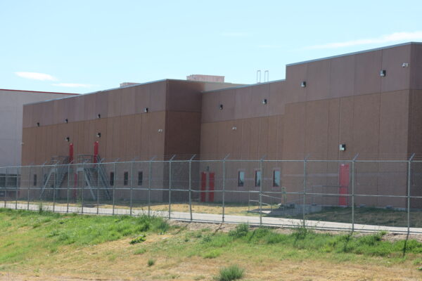Photo: outside of the ICE facility in Aurora, CO with barbed wire fences and brown concrete walls.