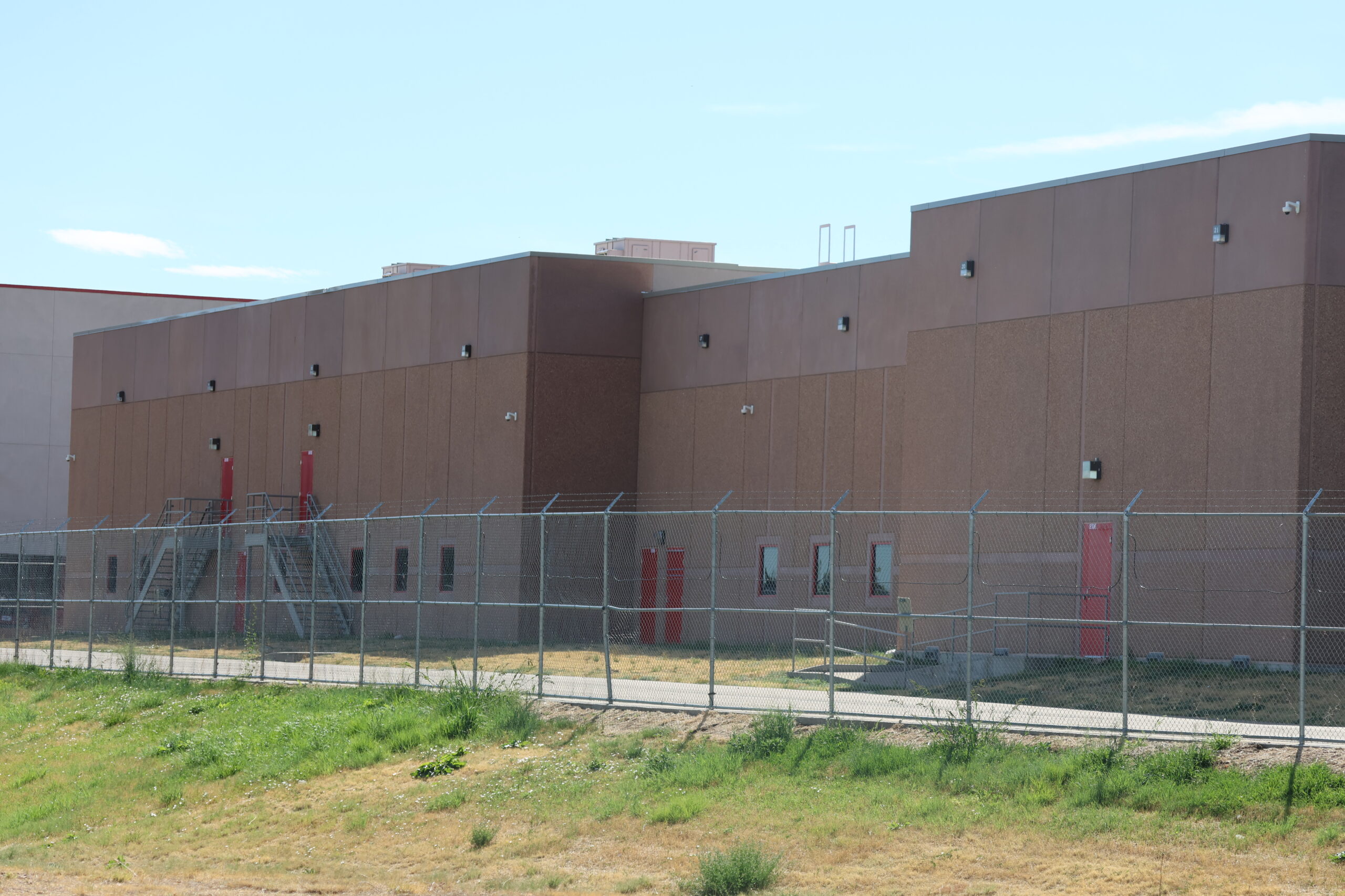 Photo: outside of the ICE facility in Aurora, CO with barbed wire fences and brown concrete walls.