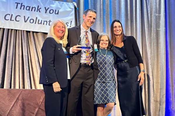 Tim Macdonald accepting Outstanding Sustained Contribution Award on a stage with 3 other people. Thank you CLC volunteers on a banner in the background.