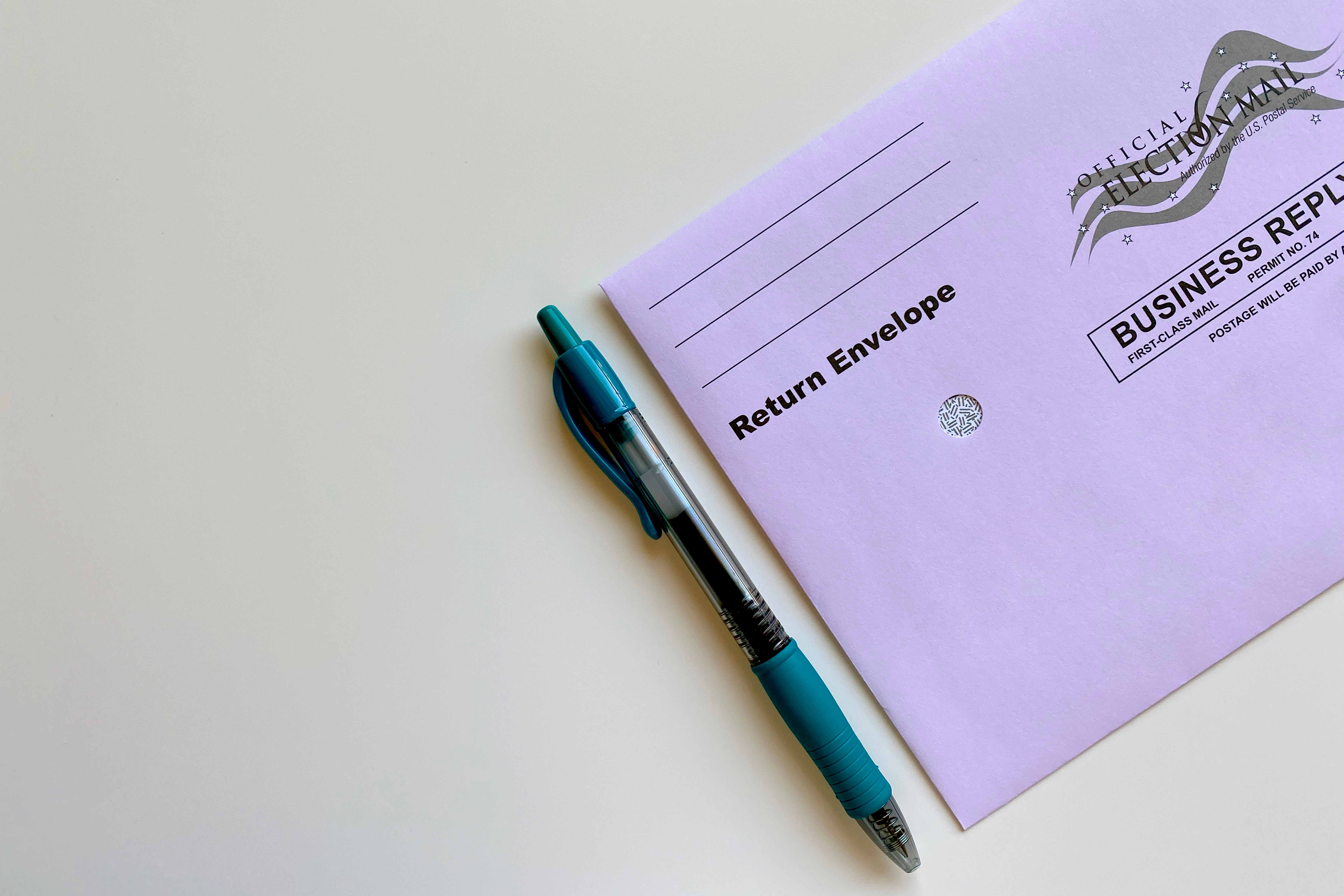 A blue pen and ballot envelope on a white surface
