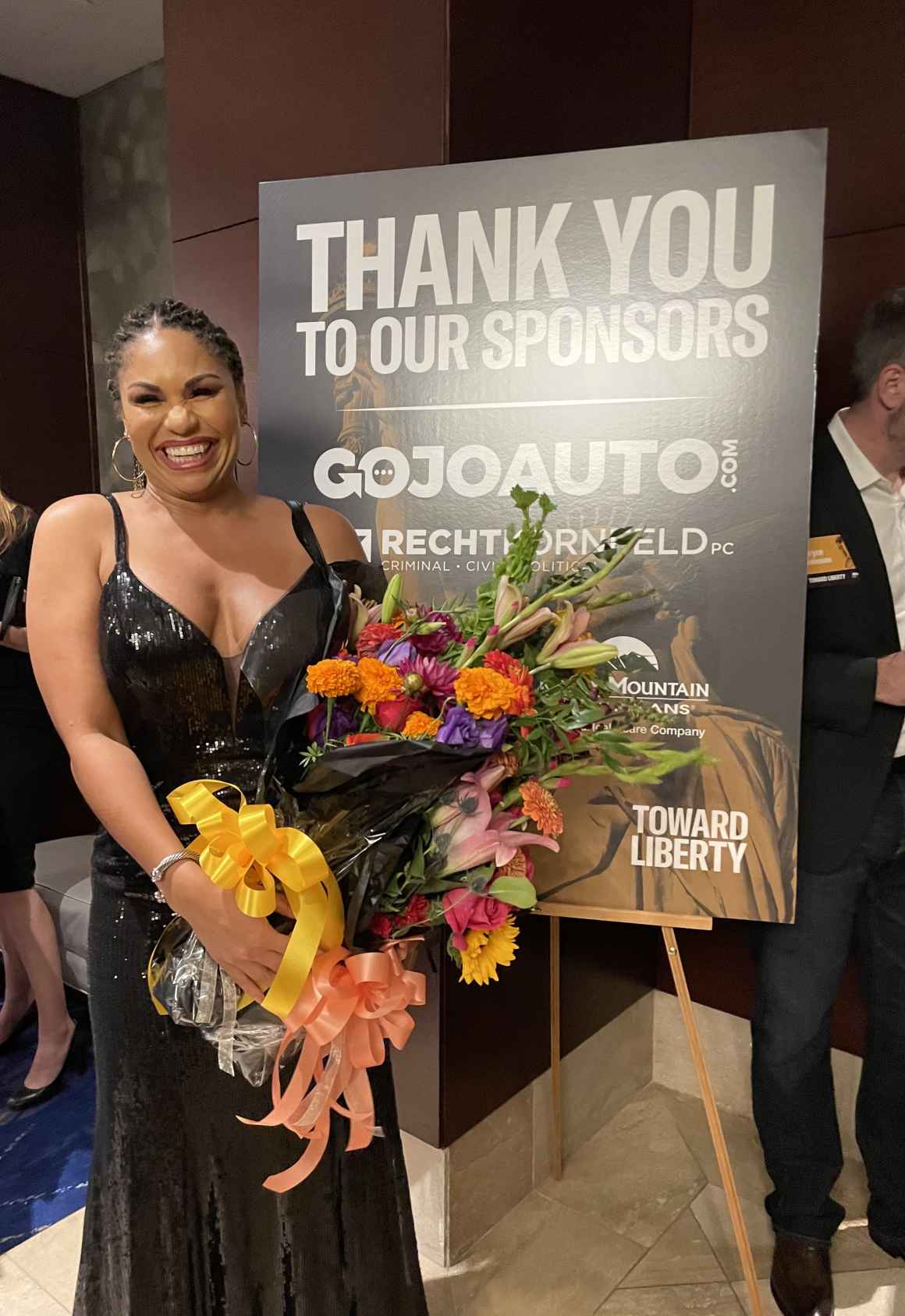 Amanda Gordon holding flowers and in front of poster with the words thank you to our sponsors
