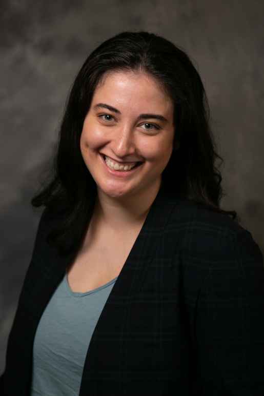 Olivia Sharp headshot, smiling, in front of gray background
