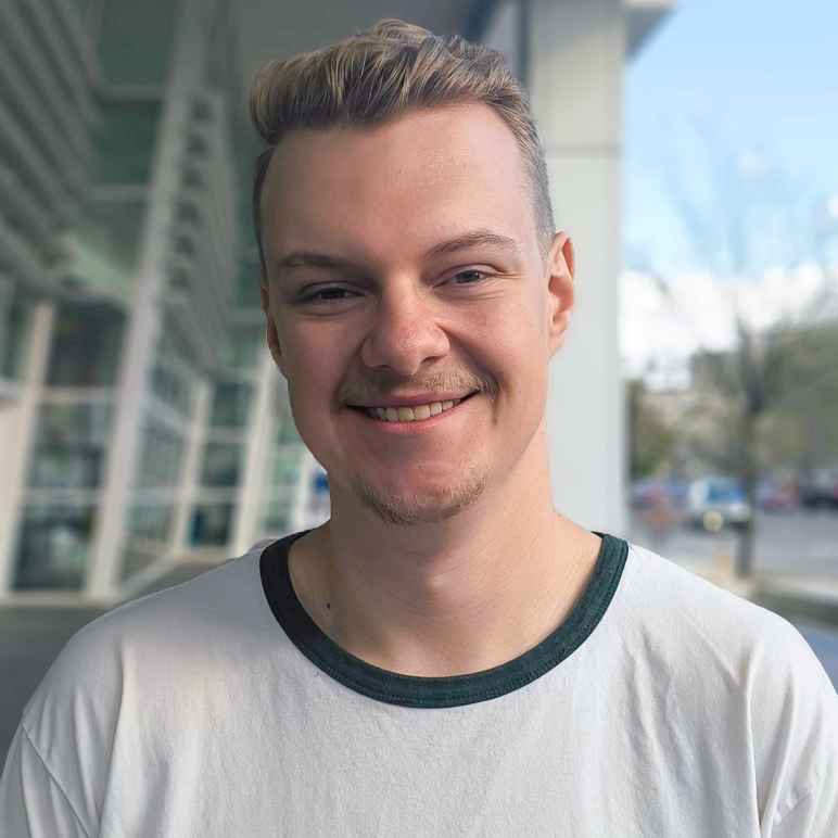 Headshot photo of Ivan, smiling, standing in front of building with large glass windows