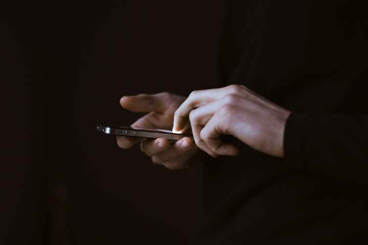 Photo of hands holding a smartphone in a dark room with a dark background