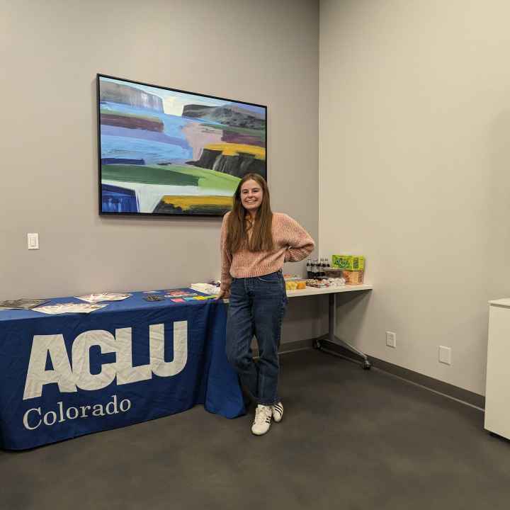 An intern stands in front of a table with a blue ACLU of Colorado tablecloth and an assortment of printed materials
