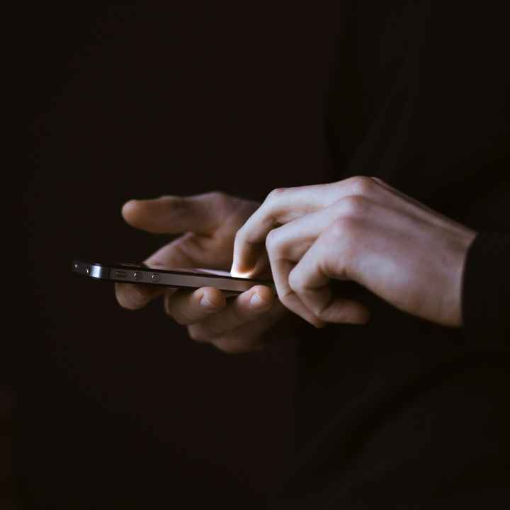 Photo of hands holding a smartphone in a dark room with a dark background