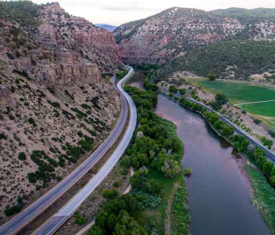 Photo of road stretching into the distance in between a cliff face and river